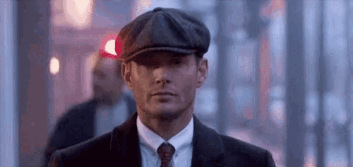 a man in a suit and tie is wearing a flat cap and looking at the camera .