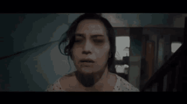 a woman with a bloody face is standing in a dark room looking up .