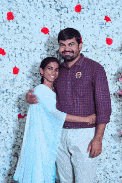 a man and a woman pose for a picture in front of a wall of white flowers
