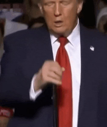 donald trump is wearing a suit and tie and pointing at something .