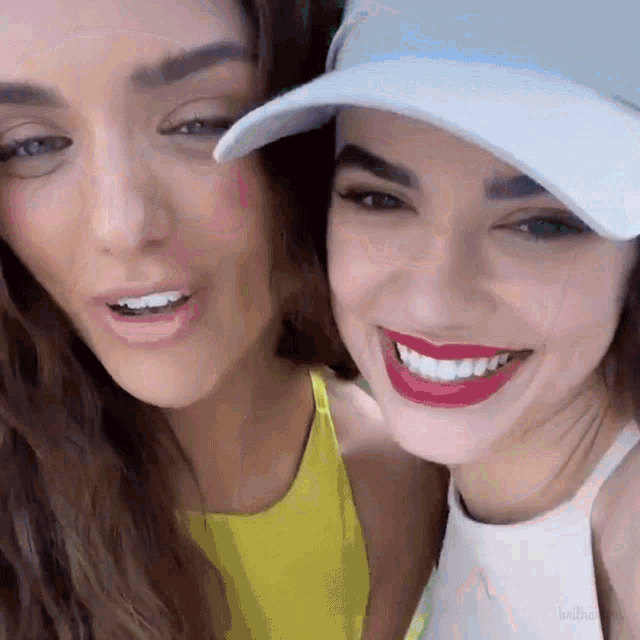 two women are posing for a picture and one is wearing a baseball cap
