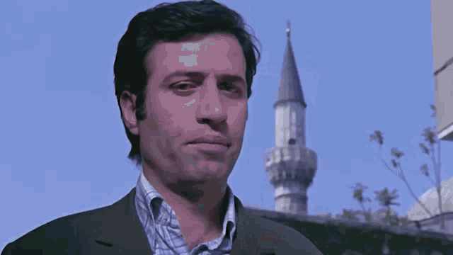 a man in a suit is walking in front of a building with a tower in the background .