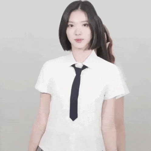 a young woman in a school uniform and tie is standing in front of a white wall .