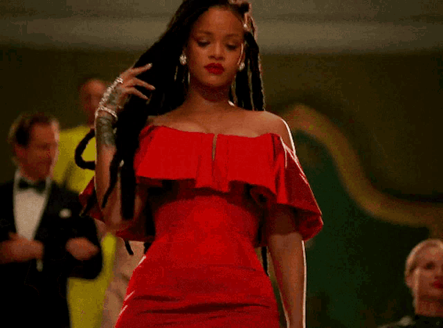 a woman in a red off the shoulder dress is standing in front of a group of people