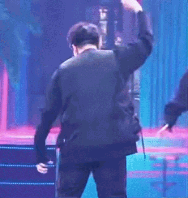 a man in a black suit is standing on a stage with a microphone in his hand .