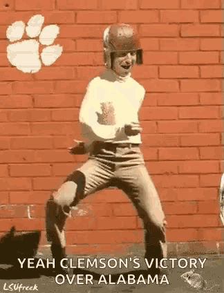 a man in a football helmet is dancing in front of a brick wall with a clemson logo on it .