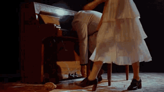 a woman in a white dress is dancing in front of a piano on a stage .