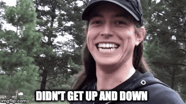 a man with long hair is wearing a hat and smiling while standing in front of trees .