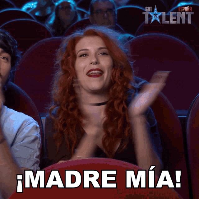 a woman with red hair applauds while sitting in a theater with the words madre mia written on the seat