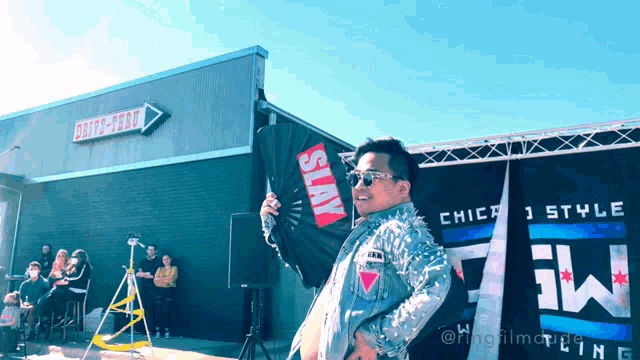 a man holding a fan in front of a building that says drive-in
