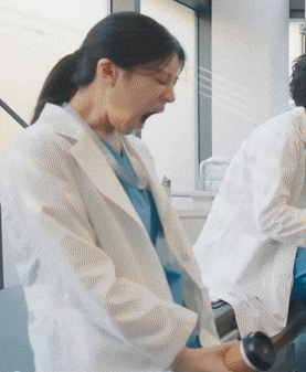 a woman in a lab coat is yawning while a man in a lab coat is using a machine .