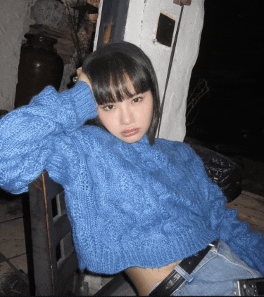 a woman wearing a blue sweater is leaning against a wall