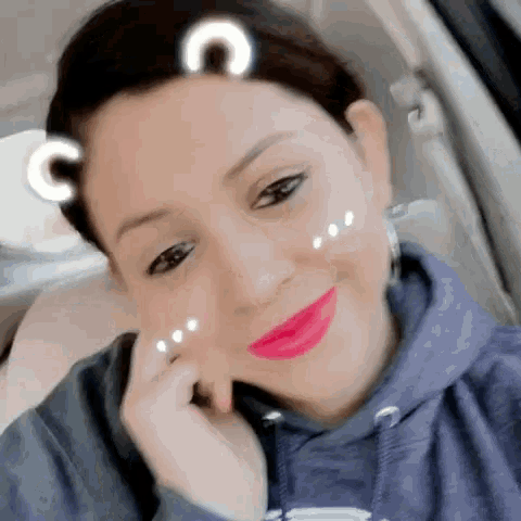 a woman wearing a purple hoodie and pink lipstick is smiling for the camera while sitting in a car .