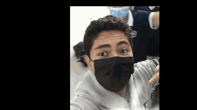 a young man wearing a black face mask is taking a picture of himself