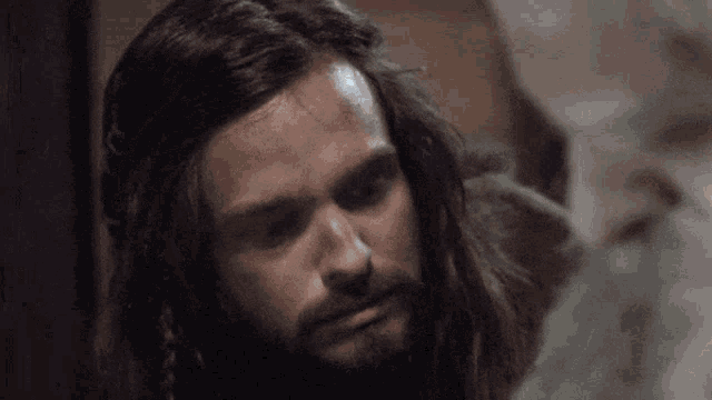 a man with long hair and a beard is looking at something