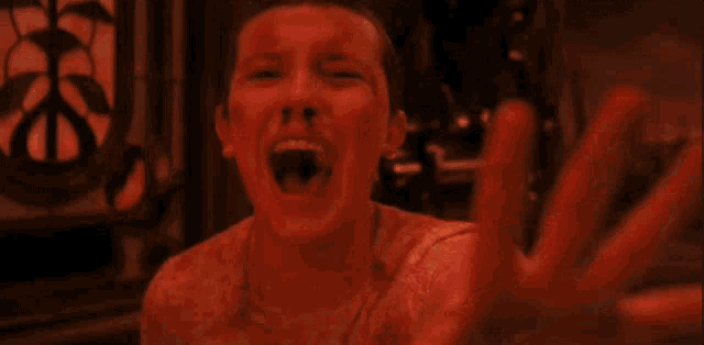 a woman with blood on her face is screaming and reaching out her hand in a red light .