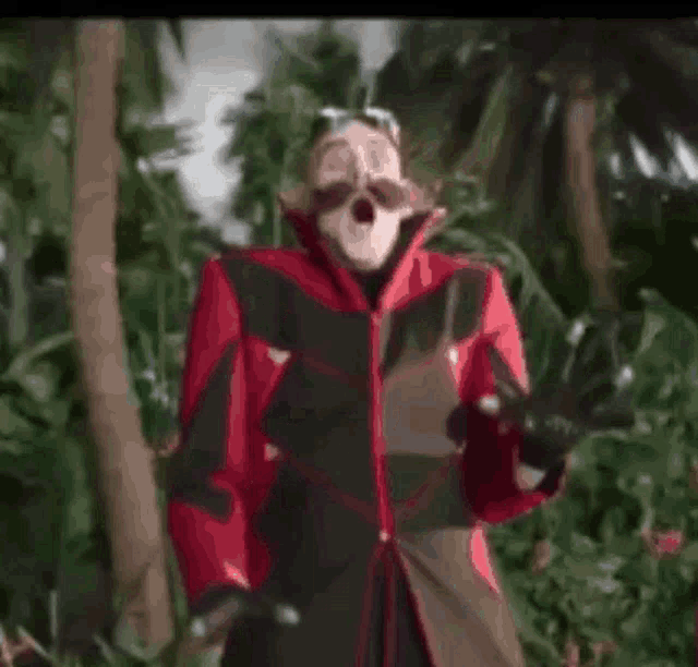 a man in a red and black jacket is standing in a jungle .