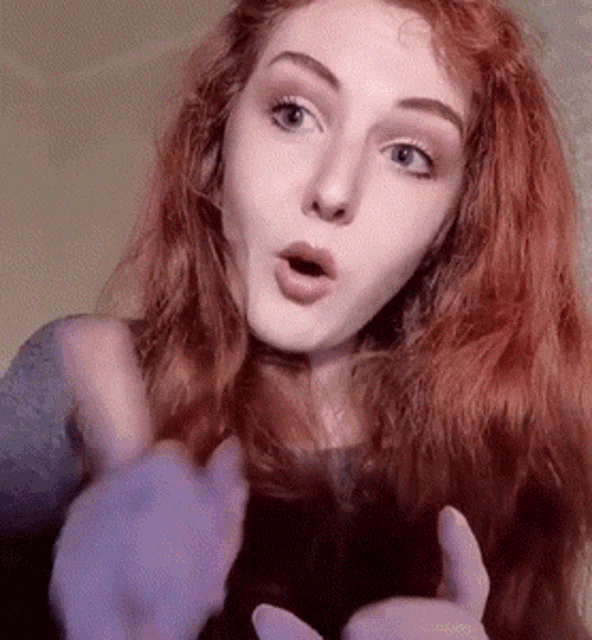 a woman with red hair is making a surprised face and giving a thumbs up