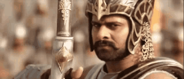 a man with a beard and mustache is holding a sword and wearing a helmet .