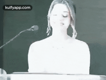 a woman is sitting at a podium with her eyes closed and a microphone in front of her .
