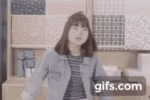 a woman in a denim jacket is dancing in a room with boxes on the shelves .