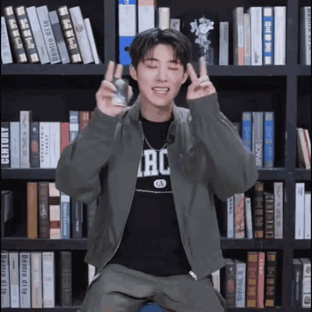 a young man sitting in front of a bookshelf wearing a shirt that says ac
