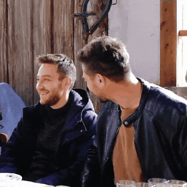 two men are sitting at a table and one is wearing a blue jacket