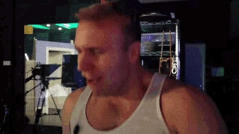 a man in a white tank top stands in front of a television