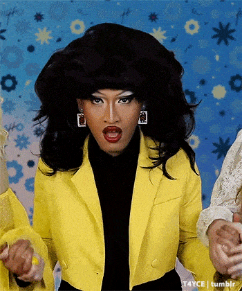 a drag queen in a yellow jacket and black turtleneck is dancing
