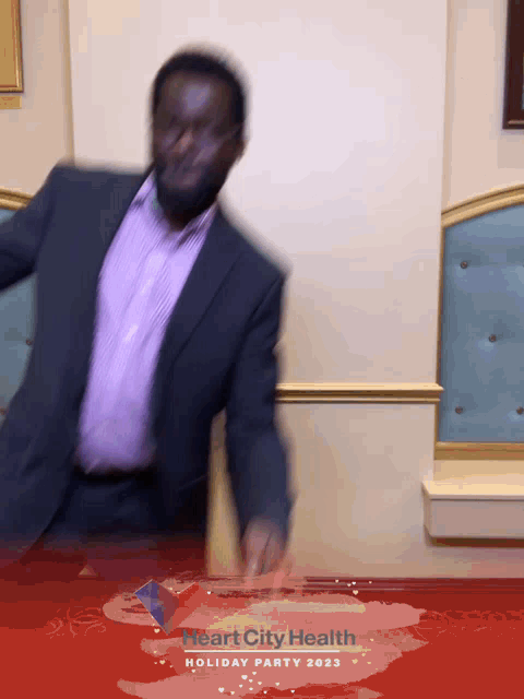 a man in a suit and a purple shirt is dancing in front of a heart city health holiday party poster