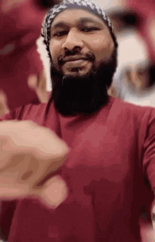 a man with a beard is wearing a red shirt and a beanie while taking a selfie .