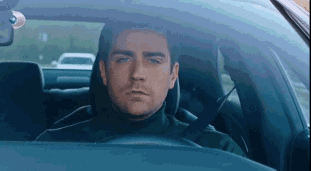 a man wearing a green turtleneck is driving a car .