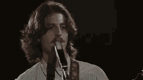 a man with long hair and a mustache is singing into a microphone while playing a guitar .