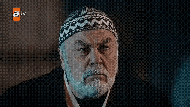 a man with a beard and a hat is making a face .