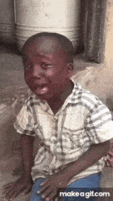 a young boy is crying while sitting on the ground and making a funny face .