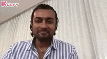 a man wearing a striped shirt and a necklace is sitting in front of a white curtain .