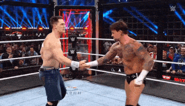 two wrestlers are shaking hands in a wrestling ring while a crowd watches .