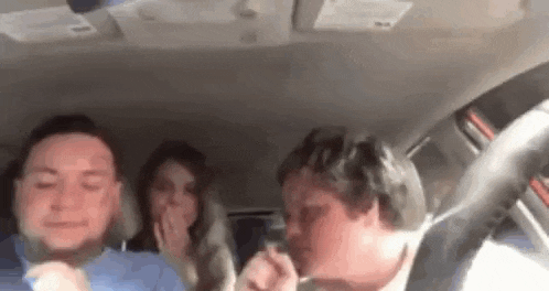 a group of people are sitting in the back seat of a car laughing .
