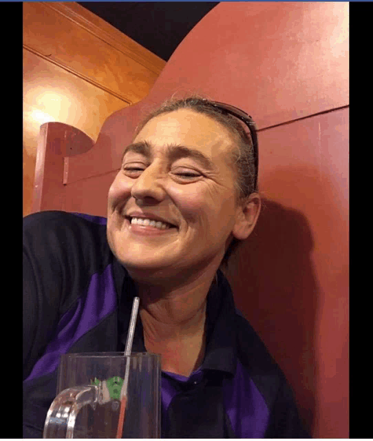 a woman in a purple shirt is smiling while holding a glass with a straw in it