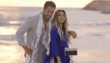 a man and a woman are standing on a beach . the woman is wearing a blue dress .