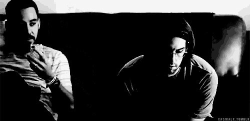 a black and white photo of two men sitting on a couch . one of the men is talking to the other .