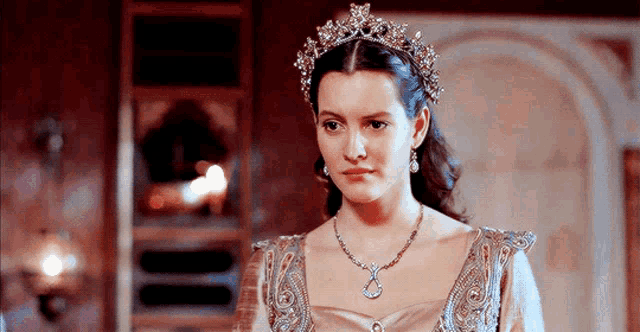 a woman wearing a tiara and a necklace is looking at the camera