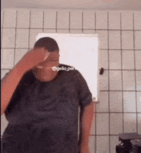 a man in a black shirt is standing in front of a window with his hand on his face .