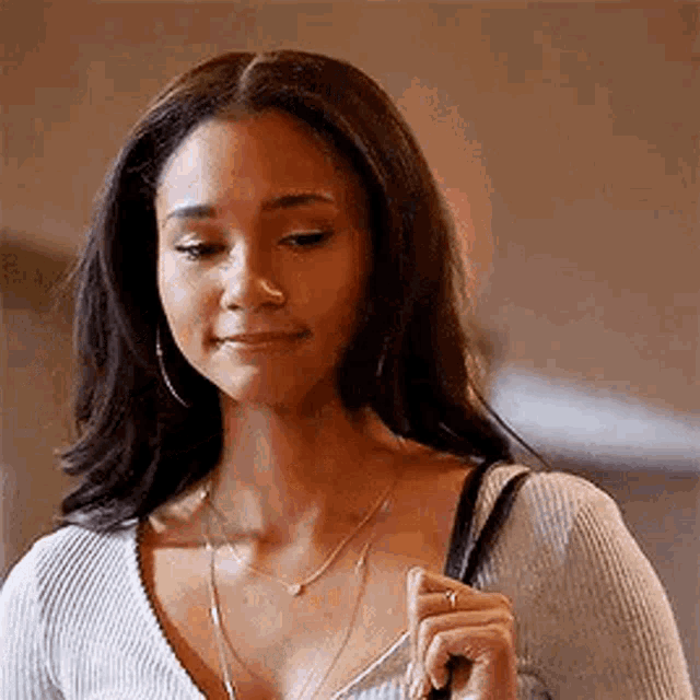 a woman wearing a sweater and a necklace is holding a purse and smiling .