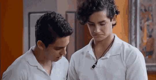two young men in white shirts are standing next to each other looking at something .