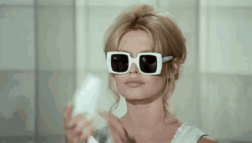a woman wearing white sunglasses and a white shirt is holding a white object .