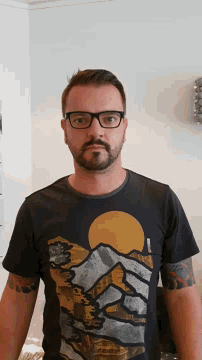 a man wearing glasses and a black t-shirt with a picture of mountains on it