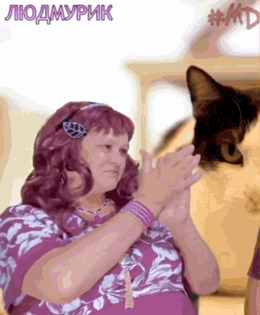 a woman in a purple dress applauds in front of a cat with #md written on the bottom