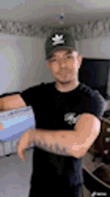 a man wearing a hat and a black shirt is standing in a room holding a box .