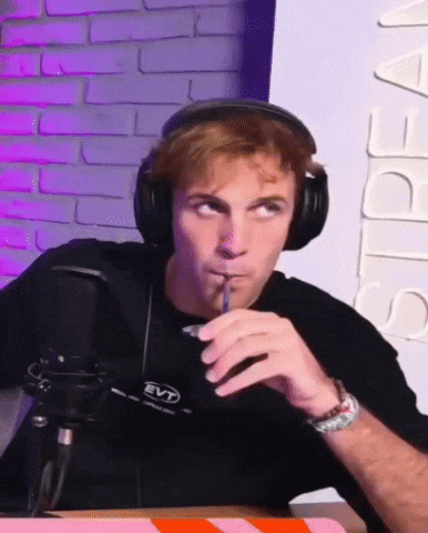a man wearing headphones is sitting in front of a microphone drinking from a cup .